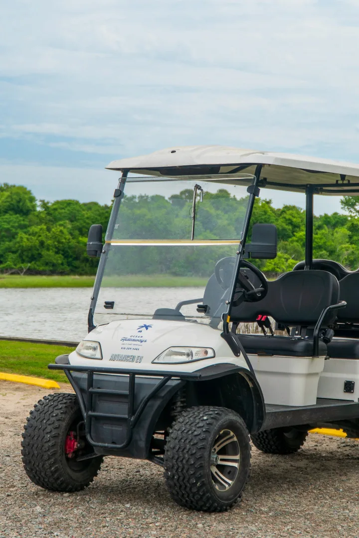 A white Ocean Hideaways golf cart parked on a gravel drive beside the waterway