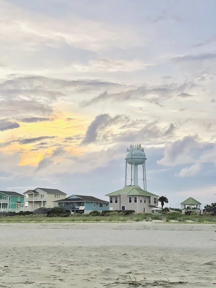 Pastel beach houses and the island water tower seen from the sand at sunset