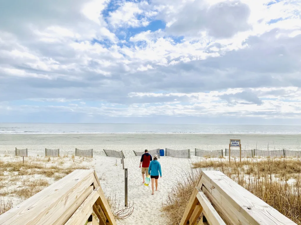 Two people walking down a wooden boardwalk onto an empty beach