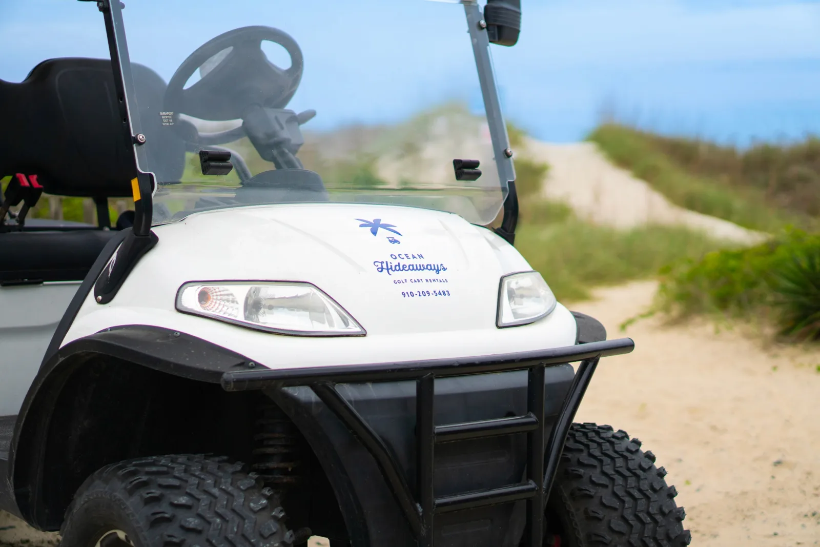 A white Ocean Hideaways golf cart parked on a sandy beach access path
